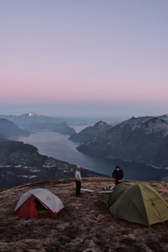 two tents set up on top of a mountain with people standing next to them at dusk