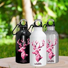 three stainless steel water bottles with designs on them sitting on a tree stump in the grass