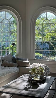 a living room with three large windows and a coffee table in front of the couch