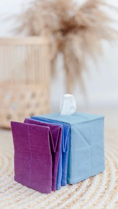 two folded napkins sitting on top of a table next to a basket with a plant in it