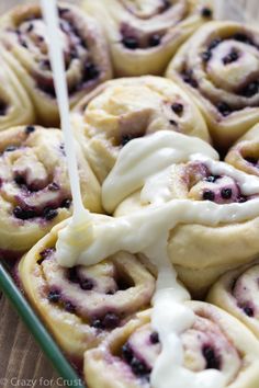 blueberry cinnamon rolls are being drizzled with white icing on a tray