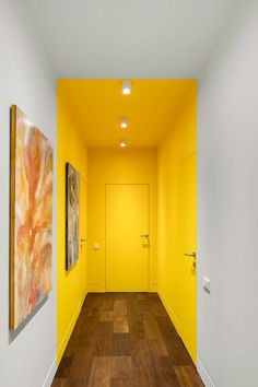 an empty hallway with yellow walls and wood flooring on the other side as well as two paintings hanging on the wall