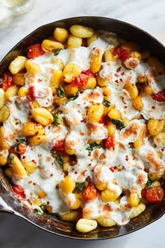 a skillet filled with pasta and sauce on top of a white countertop next to a glass of water