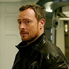 a man in a leather jacket looking off into the distance with his hand on his hip