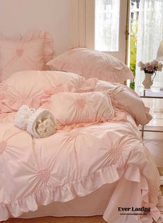 a bed with pink comforters and pillows in a room next to a window on the floor