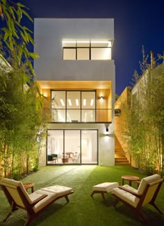 two lawn chairs sitting in front of a house at night with lights on the windows