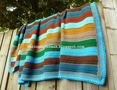 a crocheted blanket is hanging on the side of a wooden fence with a tree in the background