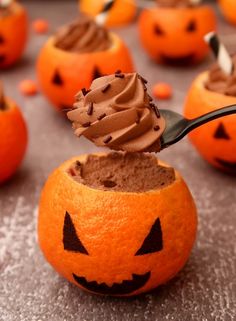 a spoon in a pumpkin cupcake with chocolate frosting on it and jack - o'- lantern faces