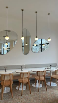 three circular mirrors hang from the ceiling in a restaurant with tables and stools around them