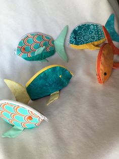 three fish made out of fabric sitting on top of a white bed sheet next to each other