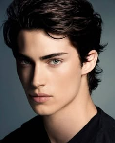 a young man with dark hair and blue eyes is posing for a photo in front of a gray background