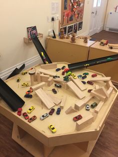 a wooden table with toy cars on it in the middle of a playroom area