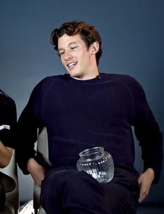 two young men sitting next to each other on a chair with a glass jar in their lap