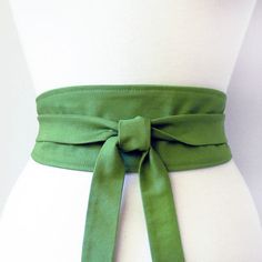 a woman's green belt with a bow on the front and side, sitting on top of a white mannequin