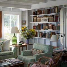 a living room filled with furniture and bookshelves next to a window covered in sunlight