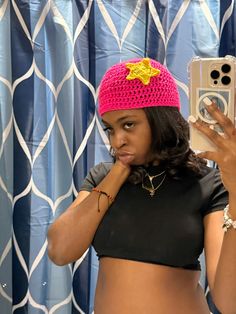 a woman in a black top is holding up her cell phone and wearing a pink crocheted hat