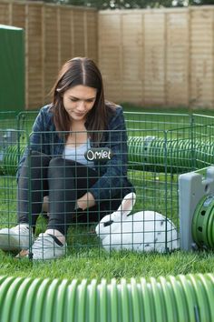 a woman sitting on the ground in front of a rabbit cage