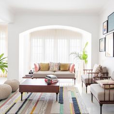 a living room filled with lots of furniture next to a large white window covered in curtains