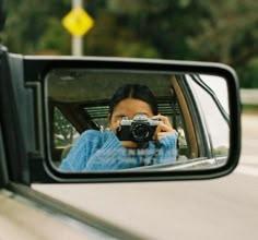 a woman taking a photo in the rear view mirror of a car with her camera