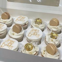 a box filled with cupcakes covered in white frosting and gold icing