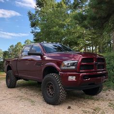 a large red truck parked on top of a dirt road next to trees and bushes