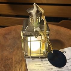 a small metal lantern sitting on top of a wooden table next to a piece of paper