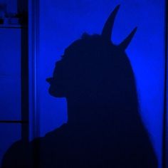 the shadow of a person with horns on their head is shown in front of a blue wall