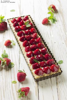 a piece of cake with strawberries on it and some leaves around the edges, sitting on a white wooden surface