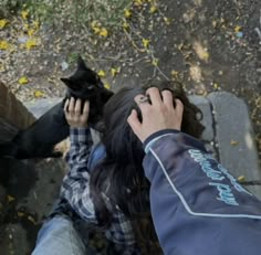 a person holding a black cat up to their face while another person pets it's head