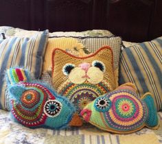 three crocheted pillows on top of a bed next to two stuffed animal fish