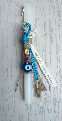 a white candle with a blue ribbon around it and an evil eye charm hanging from the end