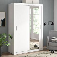 a white armoire in a living room next to a gray chair and potted plant