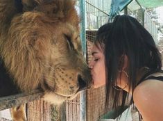 a woman kissing a lion on the nose while standing next to a caged animal