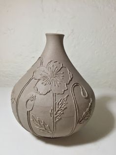 a white vase sitting on top of a table next to a wall with flowers painted on it