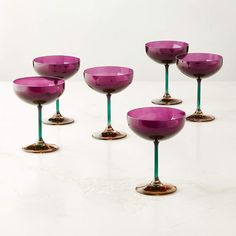 six wine goblets sitting on top of a white table next to each other