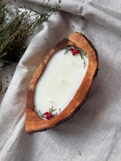 a candle in a wooden bowl on top of a white cloth next to some plants