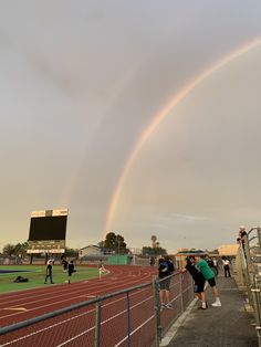 two rainbows in the sky over a track with people standing on it and watching