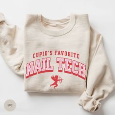 "💅 Stay cozy and stylish this Valentine's Day with our \"Cupid's Favorite Nail Tech\" Sweatshirt--a must-have for nail enthusiasts. Elevate your wardrobe and showcase your expertise with this comfortable and chic pullover, embodying the spirit of Cupid's favorite nail technician. 💅 SPECS: * UNISEX heavy blend crewneck sweatshirt (blissfully comfy); please refer to size chart in listing photos for more details * Air jet yarn for softer feel and reduced pilling * Pre-shrunk 50% cotton, 50% polyester  * Loose fit * Runs true to size * Double-needle stitched collar, shoulders, armholes, cuffs and waistband 💅 DTG PRINTING (Direct to Garment): How does it work? * With DTG printing, a printer directly applies the ink onto the t-shirt/sweatshirt with inkjet technology. It's sort of like printin Valentines Nail, Tech Gift, Tech Shirt, Nail Technician, Tech Gifts, Valentines Nails, Nail Tech, Santa Fe, Clothing Brand