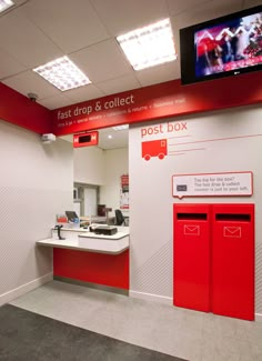 an office with red and white walls and post boxes on the wall, while a television is mounted to the wall