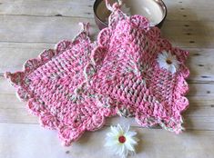 a crocheted dishcloth and two white flowers on a wooden table next to a tin