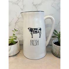 a white pitcher sitting on top of a counter next to potted plants