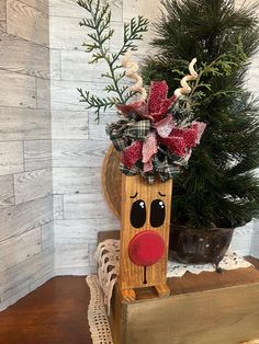 a wooden reindeer with a red nose and bow on it's head sitting next to a christmas tree