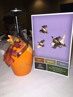 an orange vase sitting on top of a table next to a card with birds flying over it