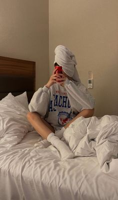 a woman sitting on top of a bed covered in white sheets holding a cell phone