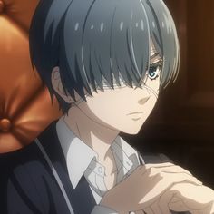 an anime character sitting in front of a chair with his hand on his chest and looking at the camera