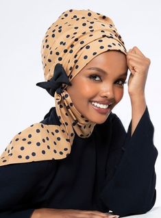 a woman wearing a polka dot head scarf and black top smiling at the camera with her hand on her hair