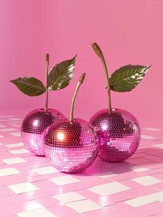 three shiny pink apples with green leaves on them