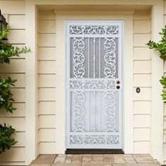 a white door with an intricate design on the side of a house next to potted plants