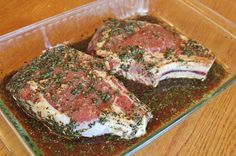 two raw meats in a glass dish on a wooden table with seasoning sprinkled around them