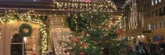 a christmas tree in front of a store with lights on the windows and decorations around it